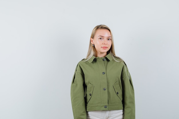 Mujer joven de pie en chaqueta verde y mirando tranquilo, vista frontal.