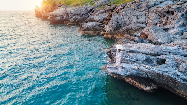 Mujer joven de pie en la cima de la roca y mirando la orilla del mar y el atardecer en la isla de Si Chang.