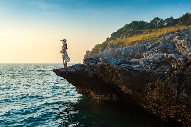 Mujer joven de pie en la cima de la roca y mirando la orilla del mar y el atardecer en la isla de Si Chang.