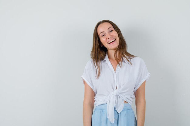 Mujer joven de pie derecho y riendo con blusa blanca y falda azul claro y mirando alegre