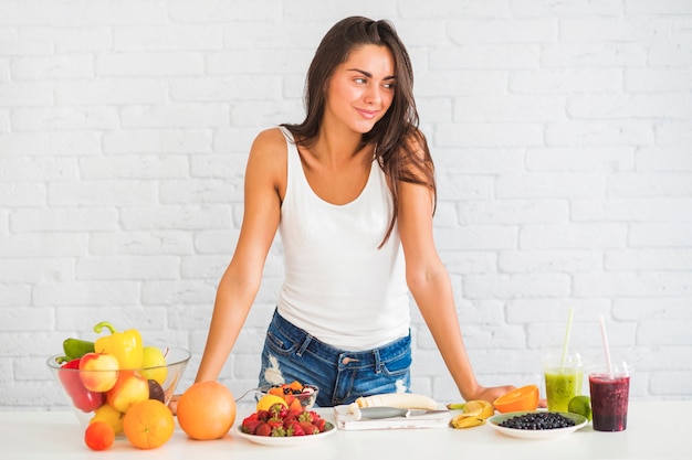 Mujer joven de pie detrás de la mesa con muchas frutas y verduras frescas