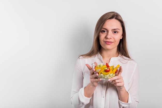 Mujer joven de pie con ensalada de verduras en un tazón