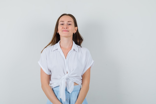 Mujer joven de pie con la espalda recta, posando al frente con una blusa blanca y una falda azul claro y un aspecto encantador