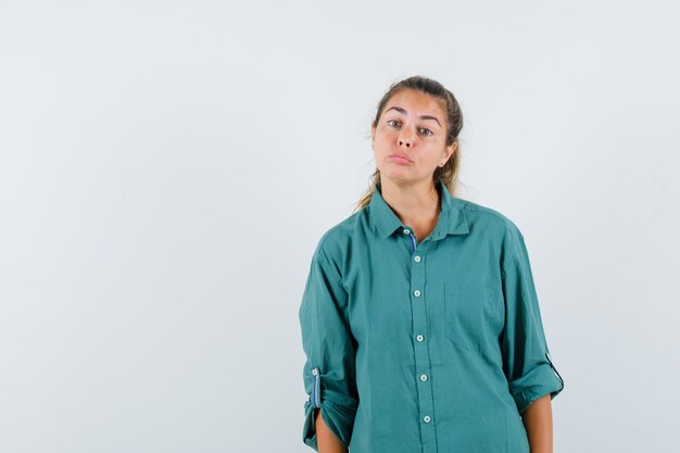 Mujer joven de pie con la espalda recta y posando al frente en blusa verde y luciendo lindo