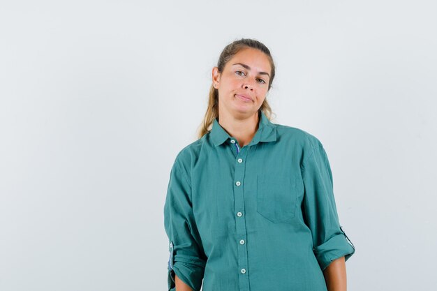 Mujer joven de pie con la espalda recta y posando al frente en blusa verde y luciendo lindo