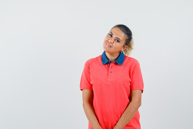 Mujer joven de pie con la espalda recta y posando en camiseta roja y mirando bonita, vista frontal.