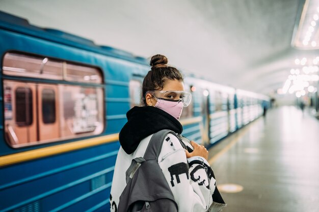 Mujer joven de pie en la estación de máscara protectora médica