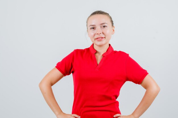 Mujer joven de pie con las manos en la cintura en camiseta roja y mirando confiado