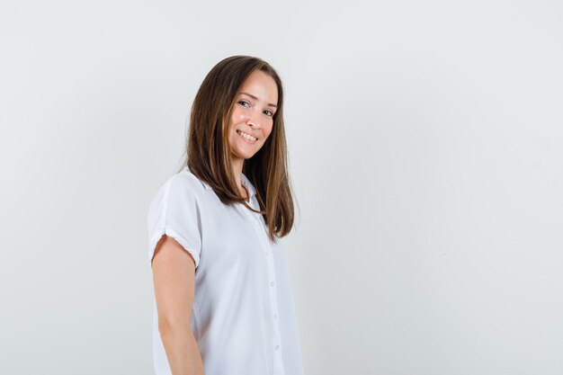 Foto gratuita mujer joven de pie mientras sonríe en blusa blanca y se ve linda