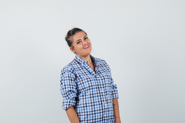 Foto gratuita mujer joven de pie mientras sonríe en camisa a cuadros y parece feliz.