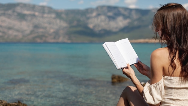 Mujer joven de pie en la orilla del mar con un libro