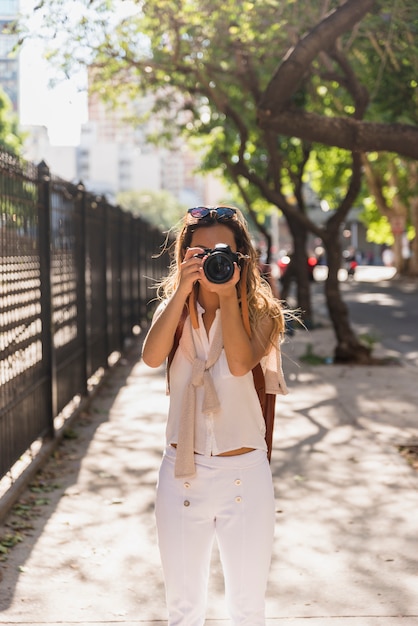 Mujer joven de pie en el parque tomando fotos desde la cámara