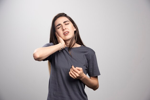 Mujer joven de pie y posando sobre un fondo gris