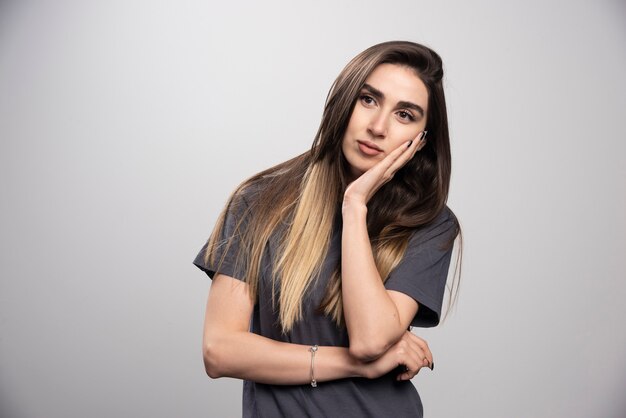 Mujer joven de pie y posando sobre un fondo gris