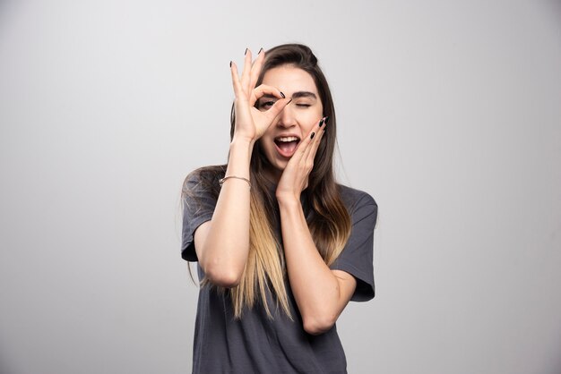 Mujer joven de pie y posando sobre un fondo gris