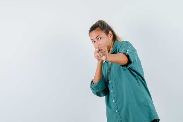 Mujer joven de pie en pose de boxeador en blusa verde y mirando lindo