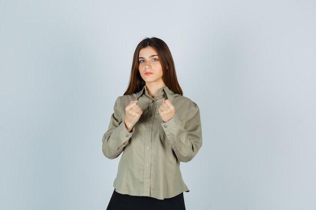 Foto gratuita mujer joven de pie en pose de lucha en camisa, falda y mirando confiado. vista frontal.