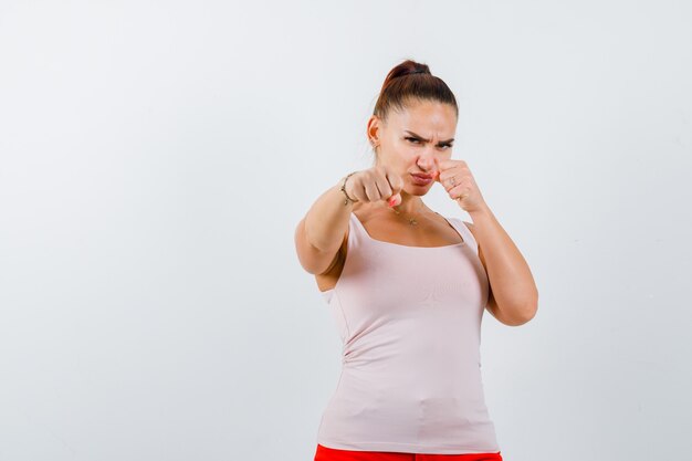 Mujer joven de pie en pose de lucha en camiseta blanca y mirando confiado. vista frontal.