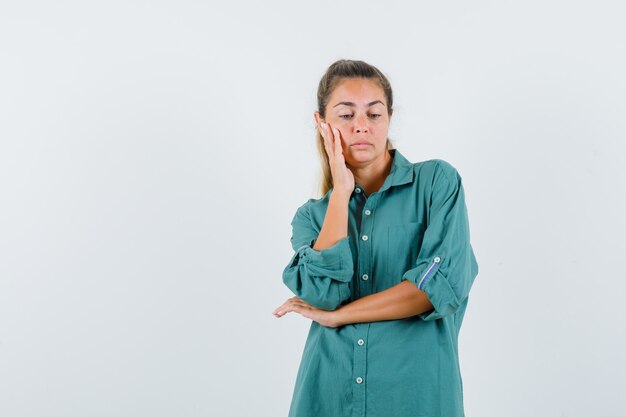Mujer joven de pie en pose de pensamiento en blusa verde y mirando pensativo