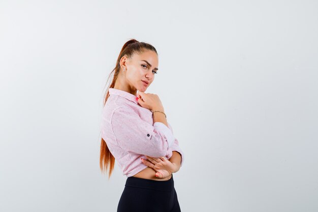 Mujer joven de pie en pose de pensamiento en camisa casual y mirando confiado, vista frontal.