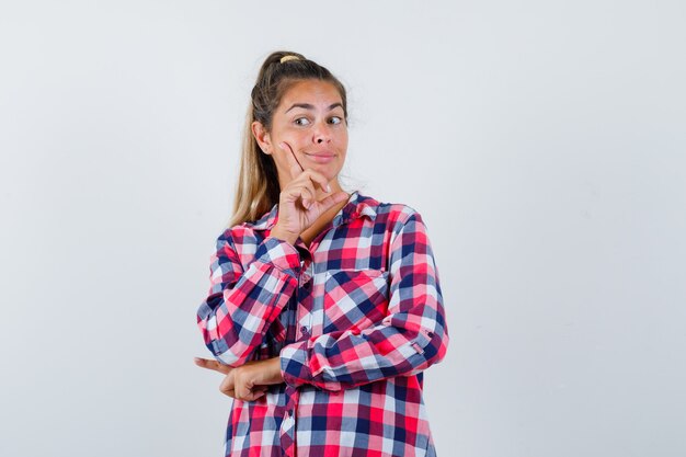 Mujer joven de pie en pose de pensamiento en camisa casual y mirando sensible, vista frontal.