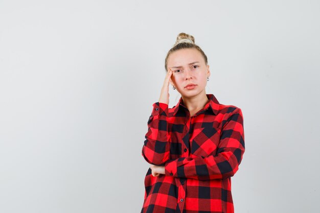 Mujer joven de pie en pose de pensamiento en camisa a cuadros y mirando triste