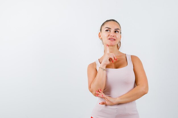 Mujer joven de pie en pose de pensamiento en camiseta y mirando considerado, vista frontal.