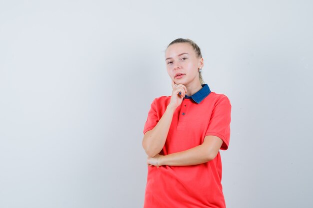 Mujer joven de pie en pose de pensamiento en camiseta y mirando sensible