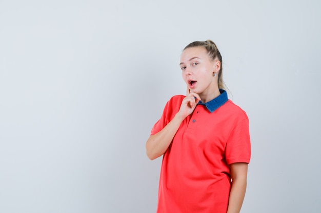 Mujer joven de pie en pose de pensamiento en camiseta y mirando sorprendido