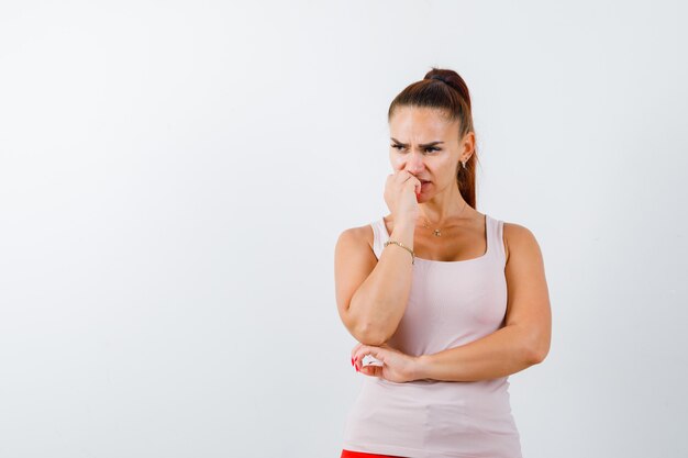 Mujer joven de pie en pose de pensamiento en camiseta y mirando vacilante. vista frontal.