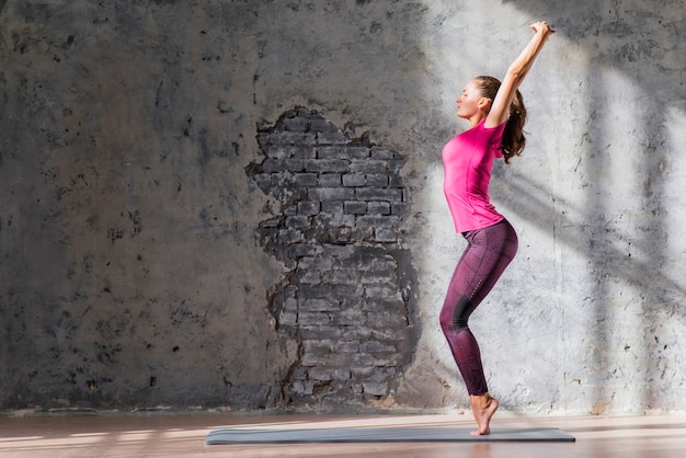 Foto gratuita mujer joven de pie de puntillas contra la pared dañada