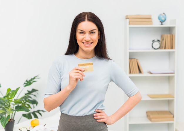 Mujer joven de pie con tarjeta de crédito en la oficina