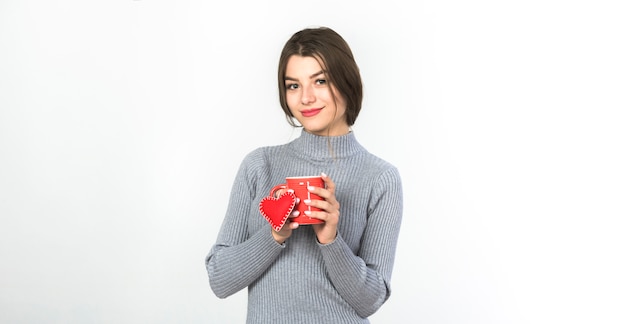 Mujer joven de pie con taza y corazón pequeño