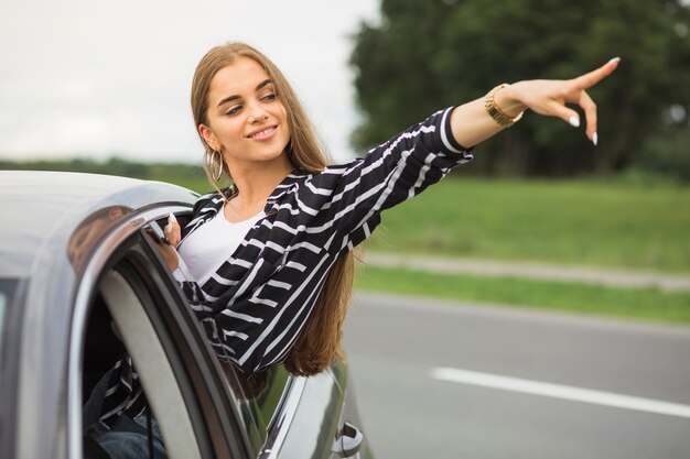 Mujer joven de pie desde la ventana del coche apuntando a algo