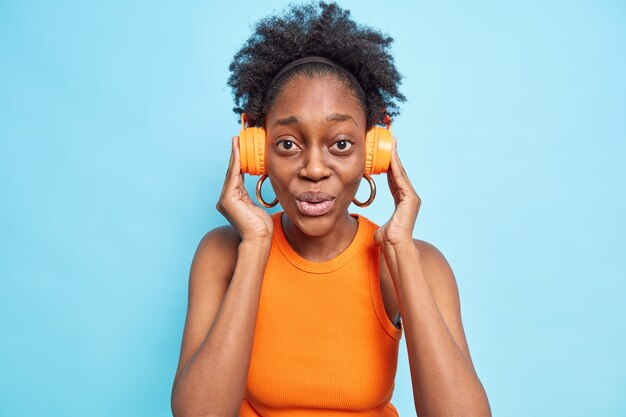 Mujer joven de piel oscura sorprendida mantiene las manos en los auriculares estéreo