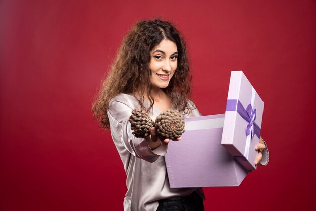 Mujer joven con piñas y caja de regalo púrpura.