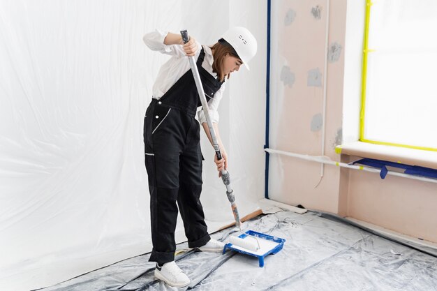 Mujer joven pintando la pared de la casa tiro completo