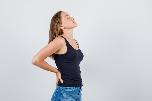 Foto gratuita mujer joven poniendo las manos en la espalda en camiseta, pantalones cortos y mirando relajado.