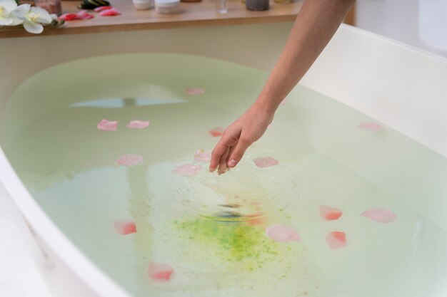 Mujer joven poniendo pétalos de rosa en el agua antes de tomar un baño