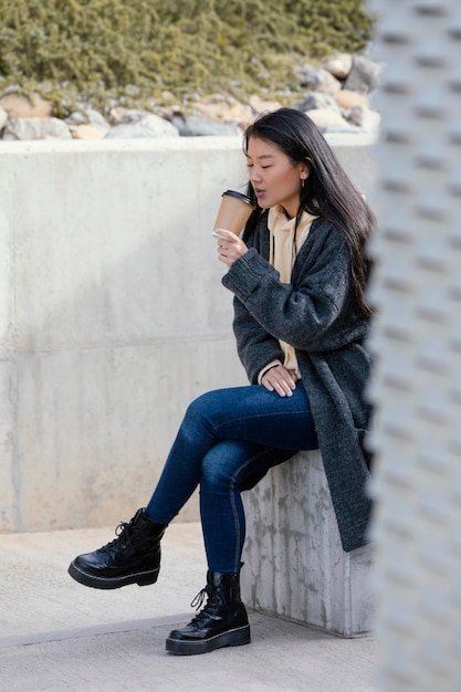 Mujer joven posando al aire libre mientras bebe café