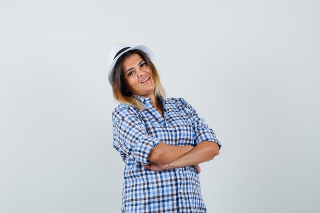 Mujer joven posando con los brazos cruzados en camisa a cuadros y mirando complacido.