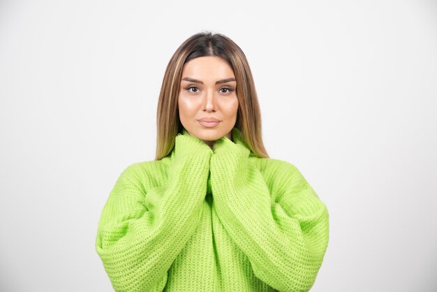 Mujer joven posando en camiseta verde sobre una pared blanca.