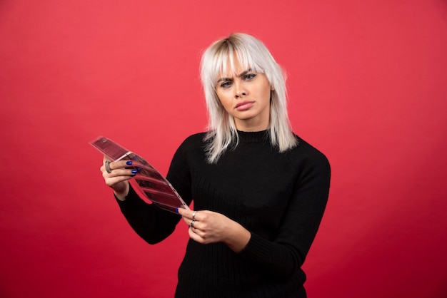 Mujer joven posando con una cinta fotográfica sobre un fondo rojo.