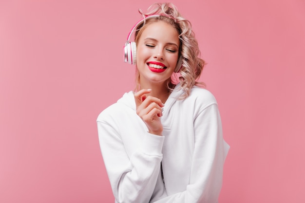 Mujer joven posando y escuchando música a través de sus auriculares rosa