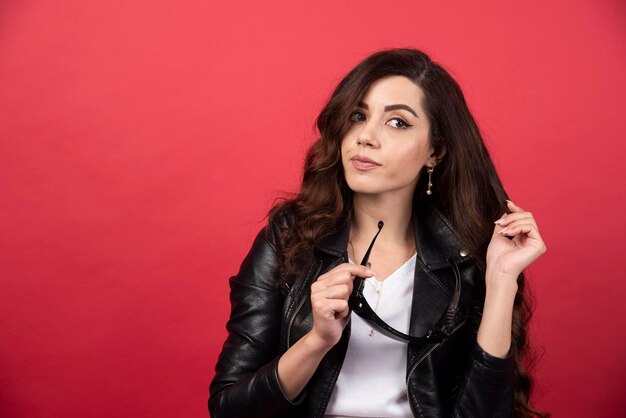 Mujer joven posando con gafas negras sobre un fondo rojo. Foto de alta calidad