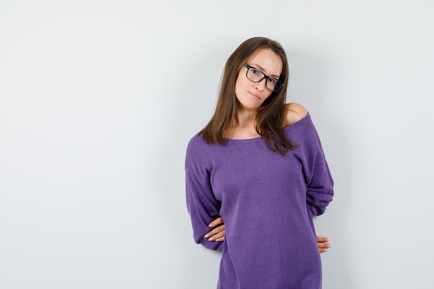 Mujer joven posando con las manos en la espalda en la vista frontal de la camisa violeta.