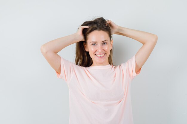 Mujer joven posando mientras arregla su cabello en una camiseta rosa y luce hermosa, vista frontal.