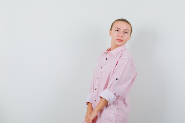 Mujer joven posando mientras está de pie en camisa rosa y mirando encantador