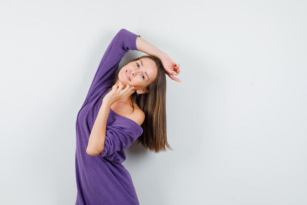 Mujer joven posando mientras está de pie en camisa violeta y parece optimista. vista frontal.