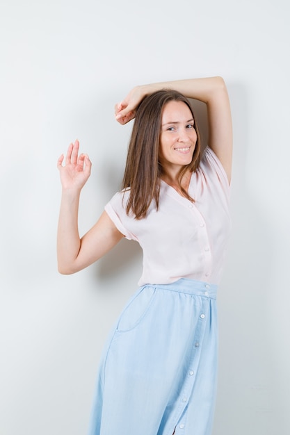 Mujer joven posando mientras está de pie en camiseta, falda y aspecto encantador, vista frontal.